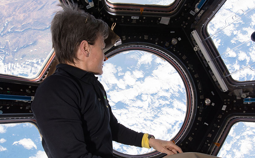 An astronaut views clouds from a window in space.