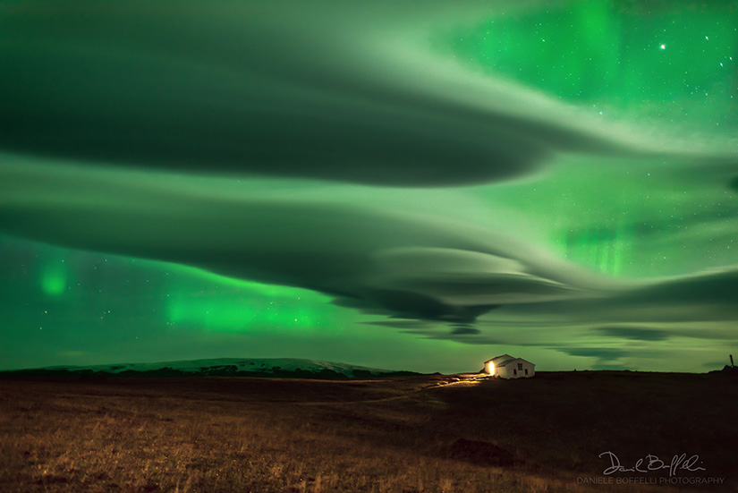 Aurora over clouds over a field and a house in Iceland.