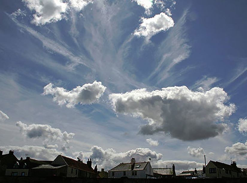 High, cold cirrus and lower, puffy cumulus clouds hover above homes.