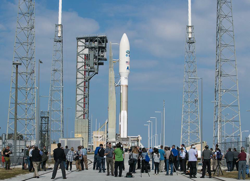 A launch vehicle sits on a launch pad with people in the foreground.