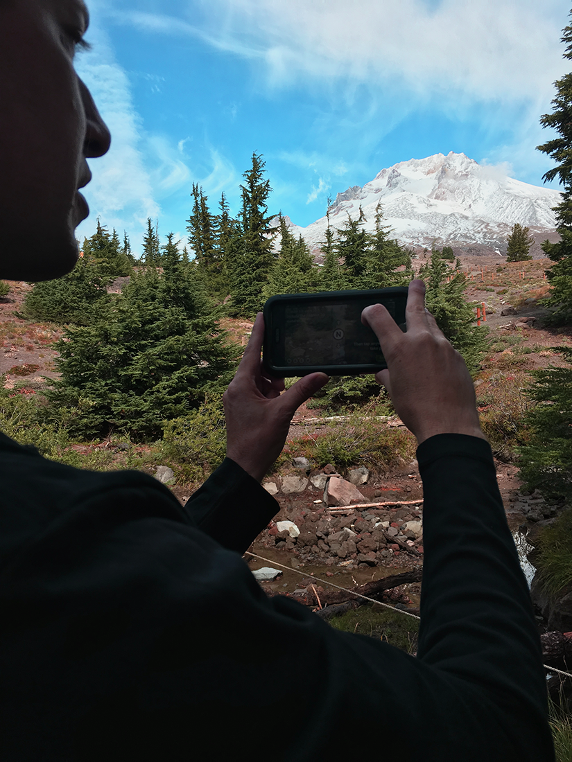 A man uses his phone to take a picture of a mountain.