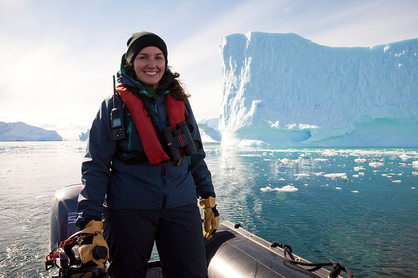 A woman stands next to a glacier.