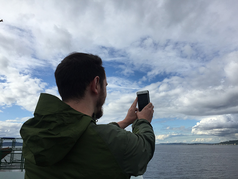 A man holds up a phone to take a picture of the clouds.