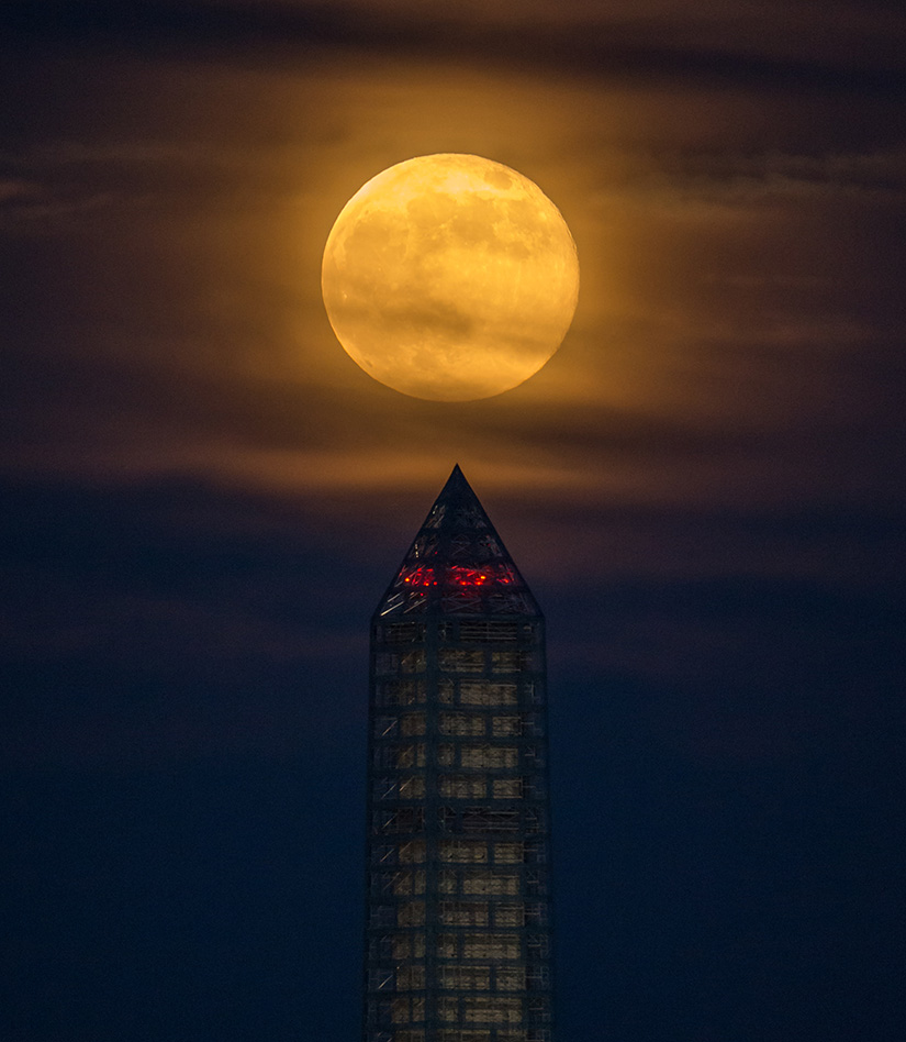 A moon rises behind a building.