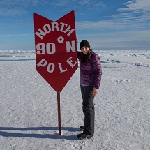 A woman stands next to a sign indicating the North Pole.