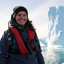 A woman stands near a glacier.