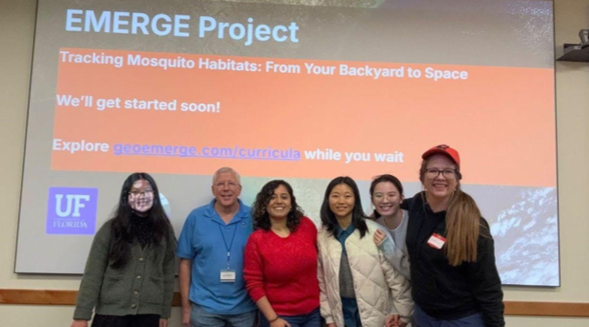 People standing in front of a projection screen with a slide titled EMERGE Project.