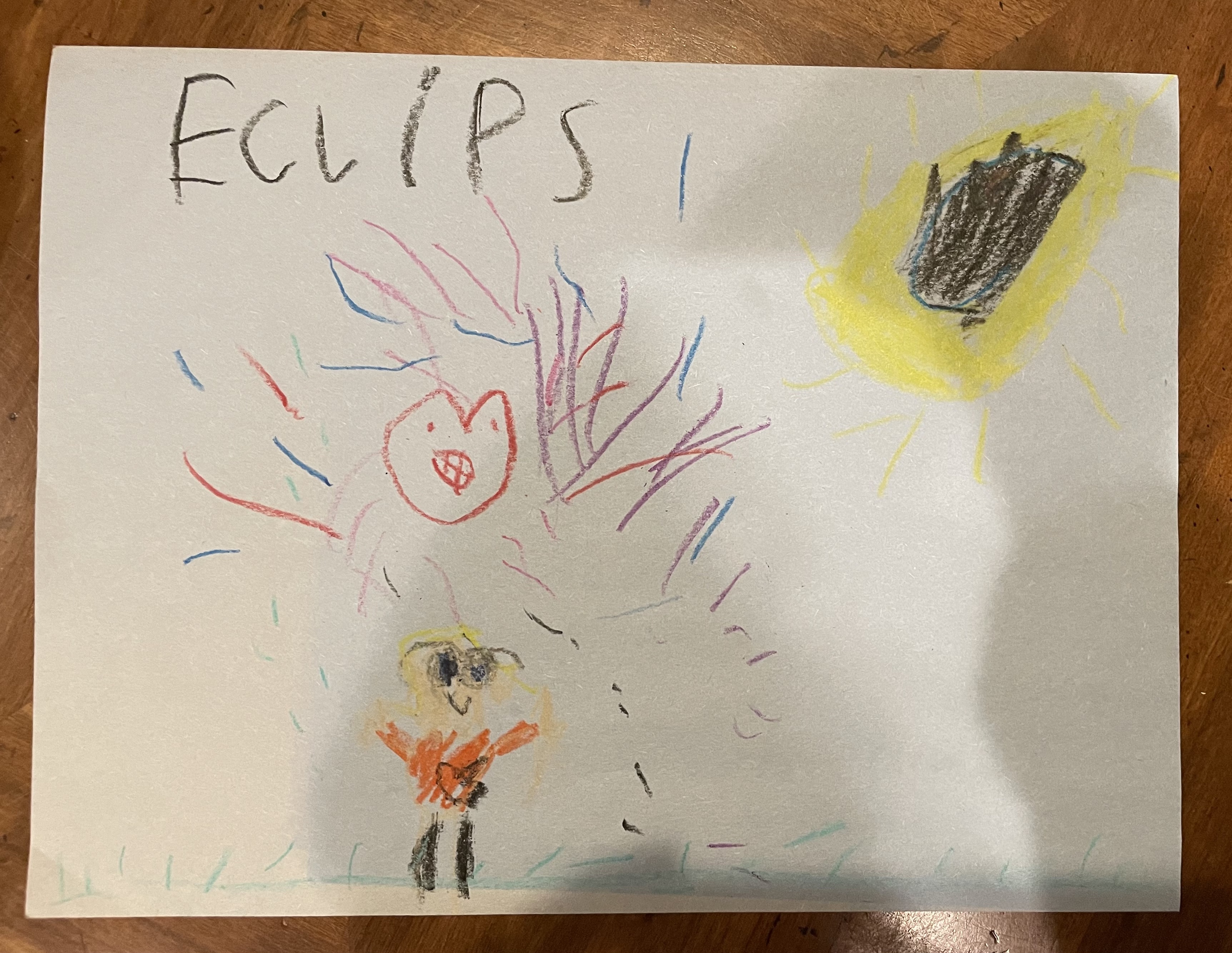 A child’s drawing of the eclipse shows the eclipsed Sun, a child wearing solar viewing glasses and a happy heart surrounded by fireworks.
