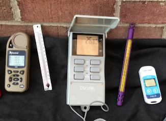 A photo showing three different digital thermometers and two alcohol thermometers on a table. 