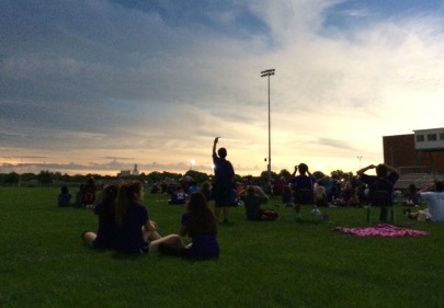 A crowd of students observe the eclipse while sitting in a school sports field. 