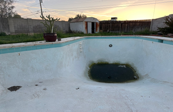 Ground-level photograph of an otherwise empty backyard pool with a large puddle of rainwater collecting in the bottom.