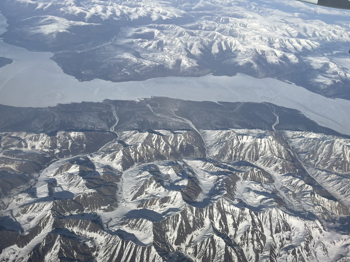 A photo showing a frozen river running between snow-covered mountain ranges taken from an airplane. 