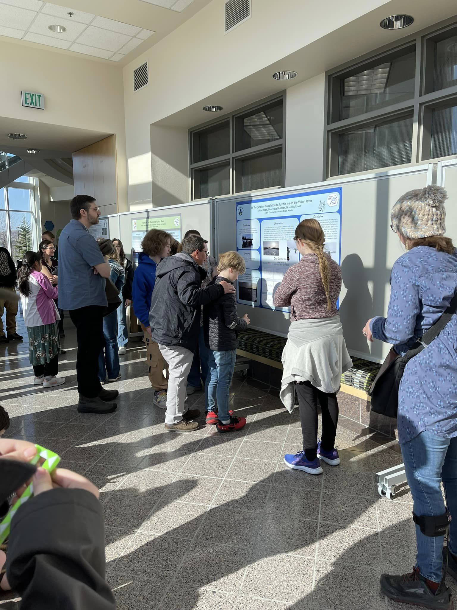 Several adults and students are gathered around a series of posters and talking. 