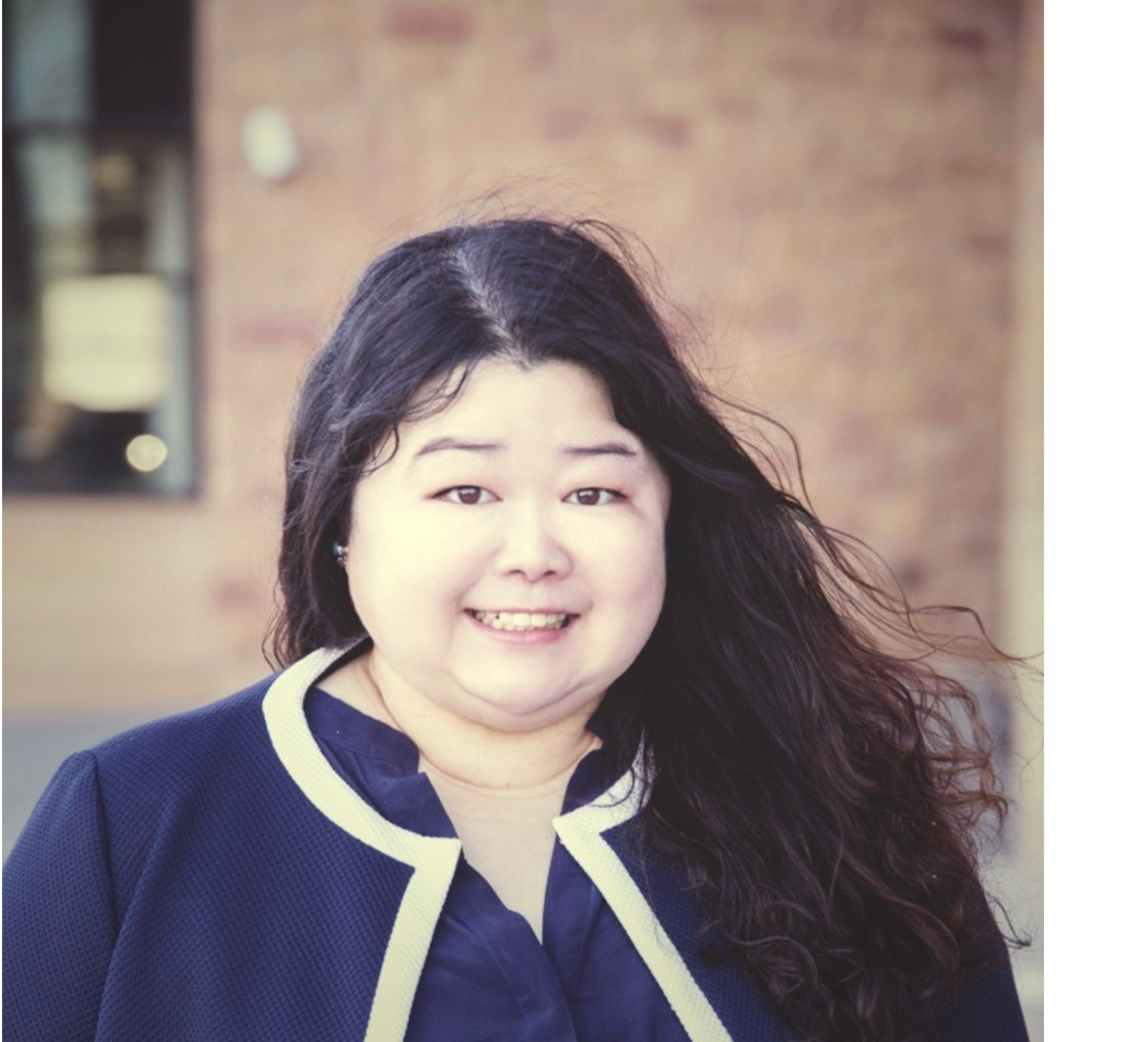 A photo of a woman with long, black hair. She is smiling and wearing a blue blouse and suit jacket. 