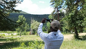 A man holds a smartphone up to the sky.