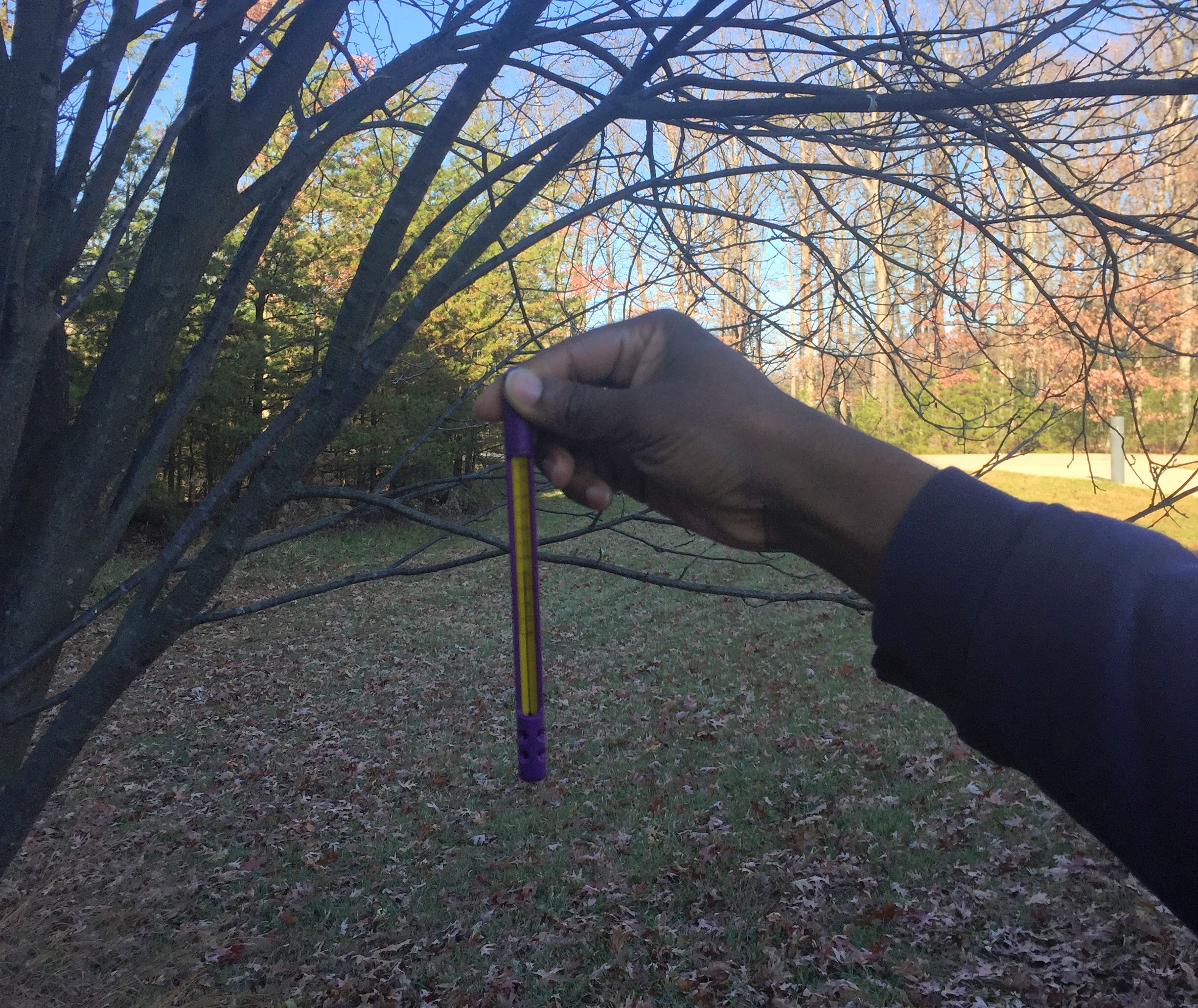 Hand holding a thermometer in the shade.