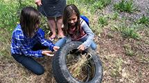 Two girls dumping out rainwater collected in a discarded tire.