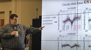 A man points at a screen with graphs of clouds and air temperature.