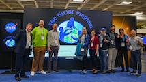 A row of people stand in front of a screen with the GLOBE Program logo on it.