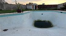 Ground-level photograph of an otherwise empty backyard pool with a large puddle of rainwater collecting in the bottom.