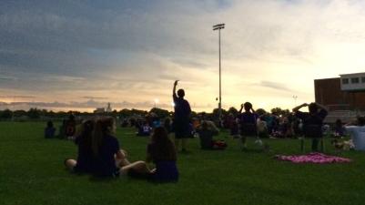 A crowd of students observe the eclipse while sitting in a school sports field.