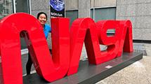 Intern Jessica Mo standing behind NASA logo sign.