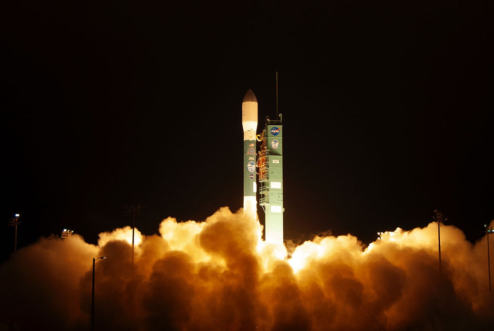 Against the background of a dark sky, a rocket has smoke and steam billowing from it's base as it prepares to separate from the launch toward and propel itself into space.