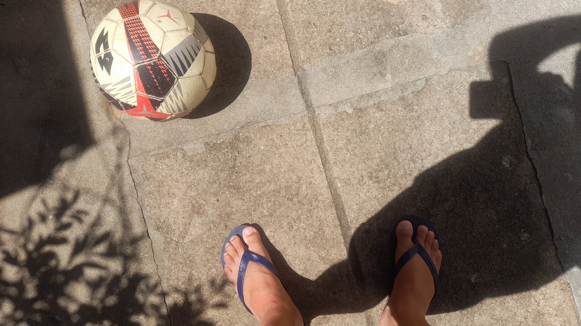 Soccer ball on a pavement surface with feet in flipflops.
