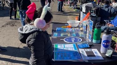 A child looks at a table that holds information about GLOBE Eclipse during an outdoor event.